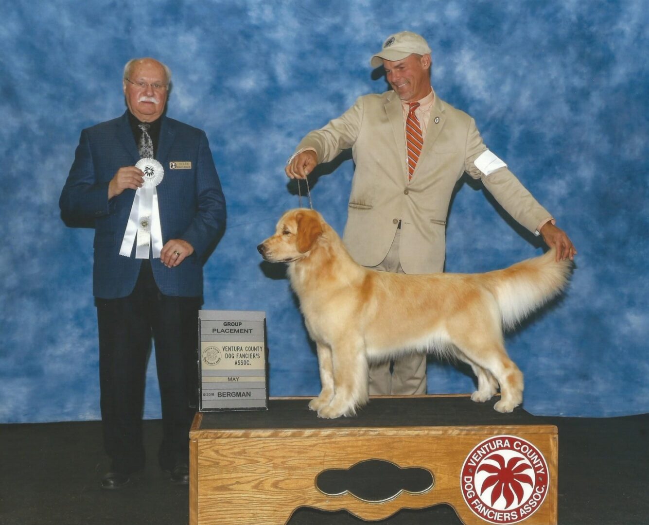Two men standing next to a golden retriever at a show.