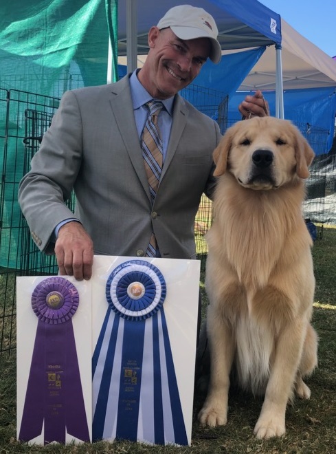 A man poses with a golden retriever at a dog show.