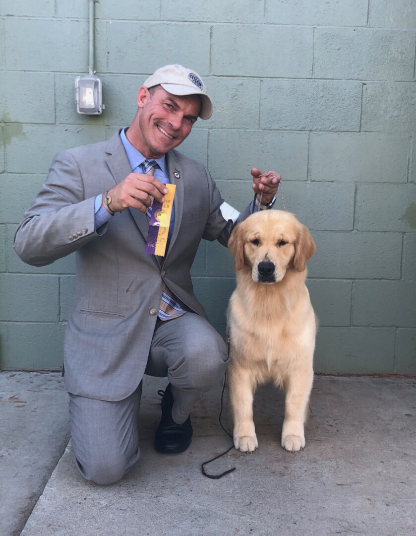 A man in a suit and tie poses with a golden retriever.