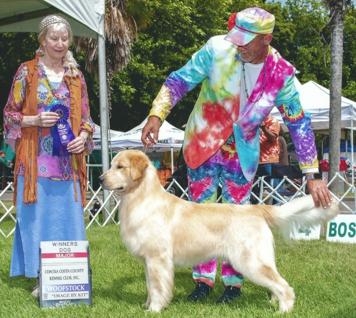 Two people standing next to a golden retriever at a dog show.